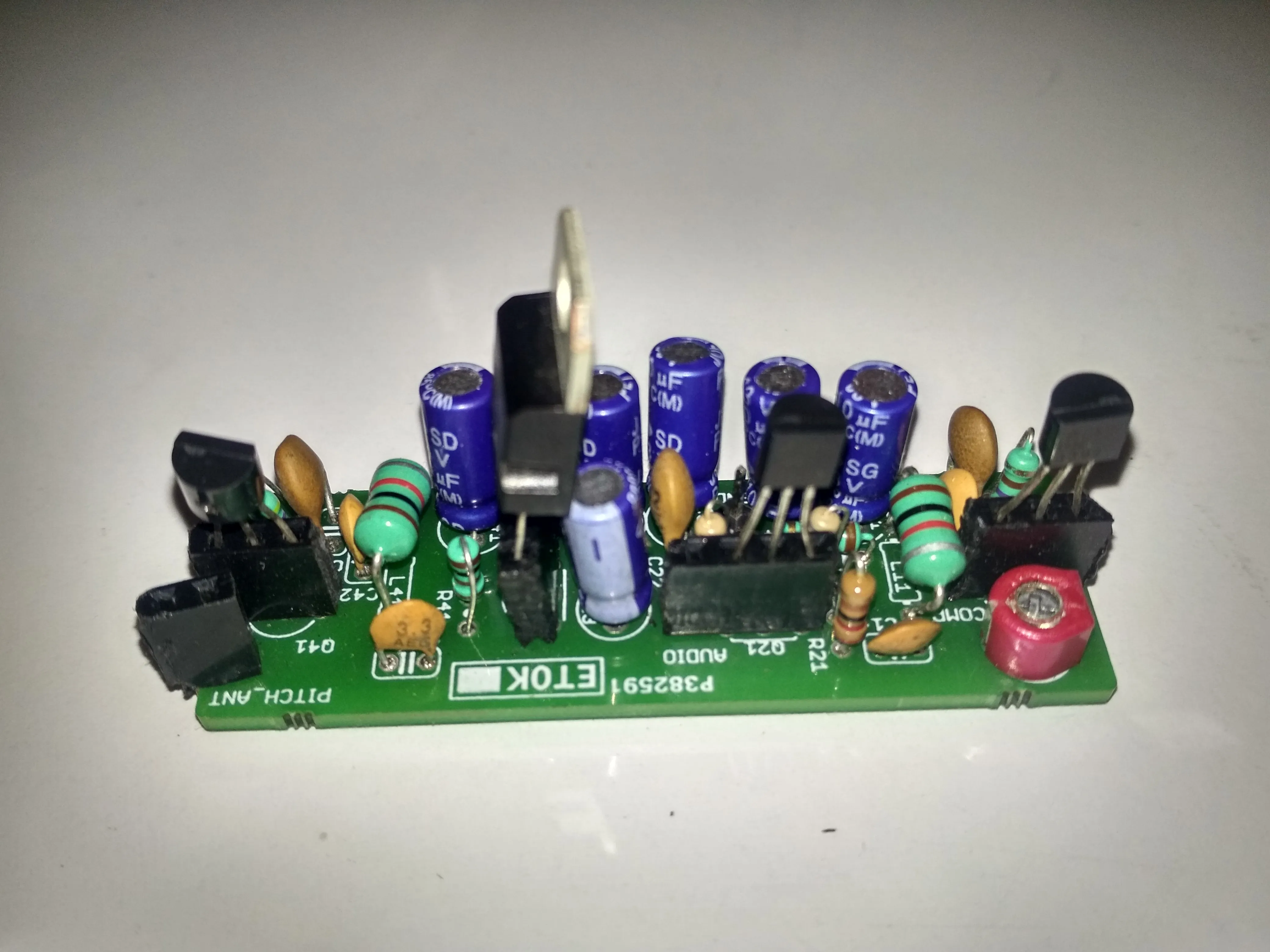 The fabricated theremin PCB, populated with JFETs, inductors, and electrolytic capacitors, silkscreened with PITCH_ANT and AUDIO labels